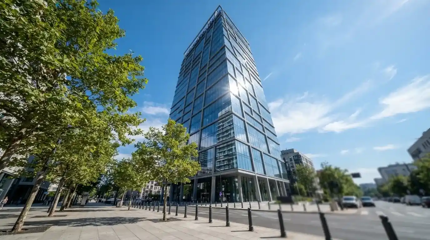Edificio moderno de oficinas con grandes ventanales de cristal reflejando el cielo, visto desde una calle peatonal.