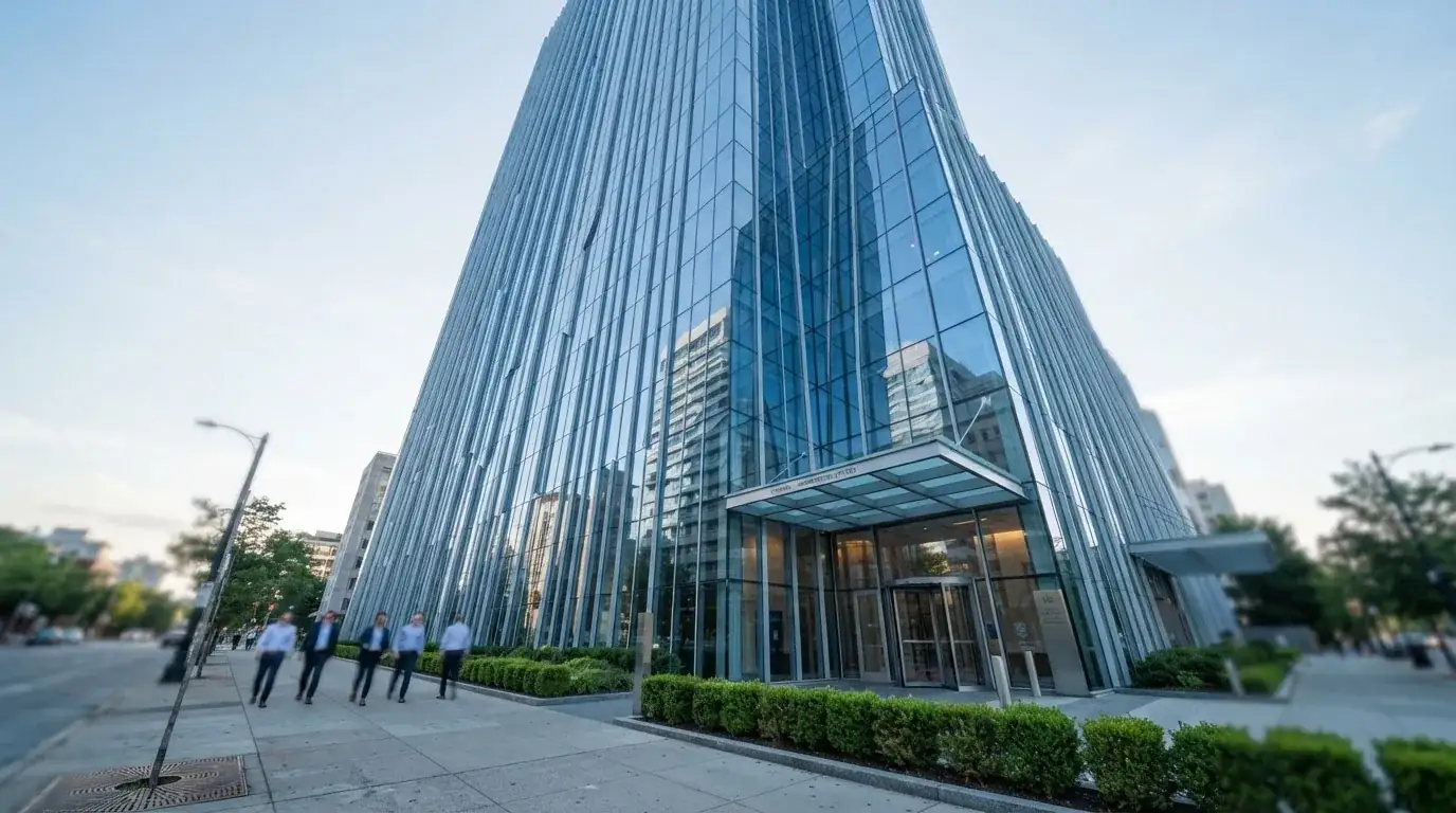 Un edificio de oficinas con fachada de cristal reflejando el cielo, fotografiado desde la acera de una calle ancha.